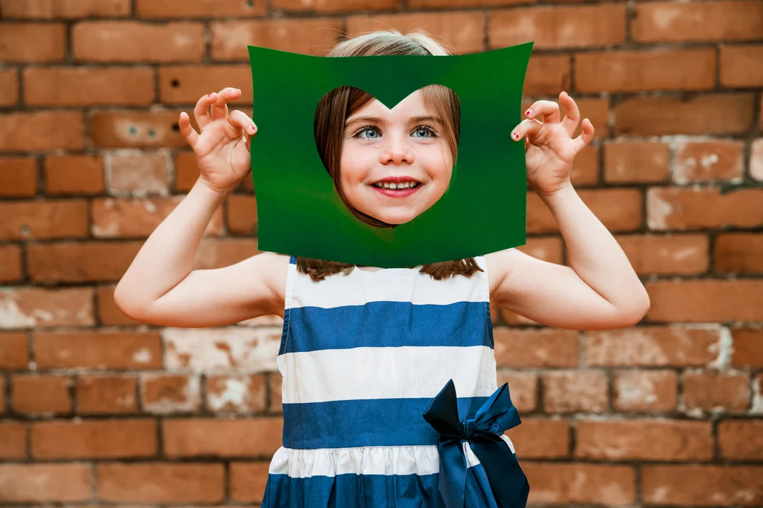 Criança sorridente a segurar uma moldura verde em forma de coração